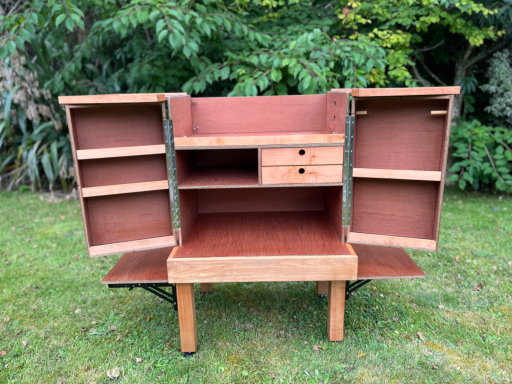 Wooden cabinet with open doors and shelves, resting on a green lawn.